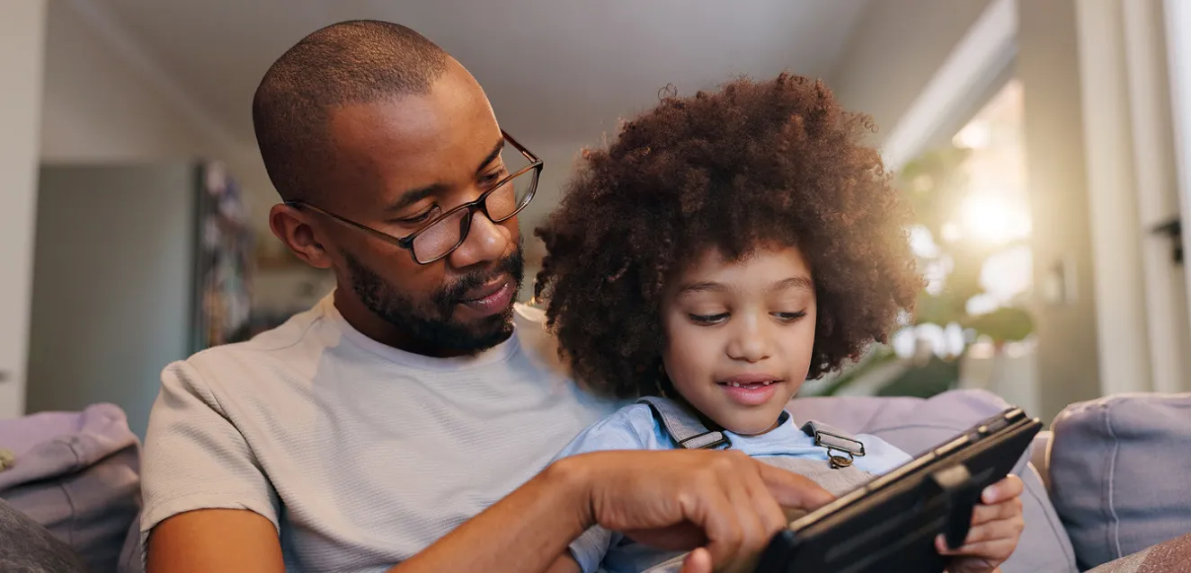 An adult with a child on his knee both engaging with a technological device
