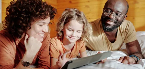 2 adults smiling whilst watching a young person use an electronic device