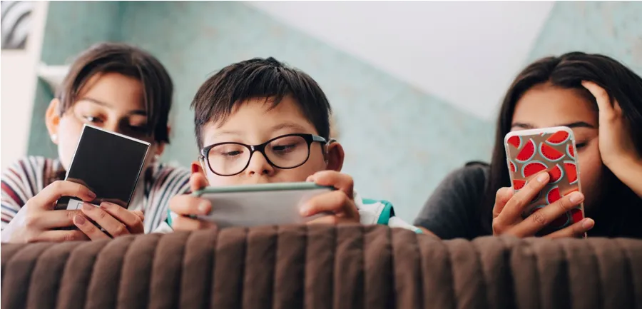 An image of three young children leaning on a sofa looking at and using mobile phones