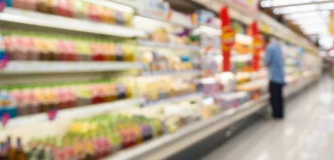 Blurry image of a person looking into a large fridge filled with drinks in a supermarket
